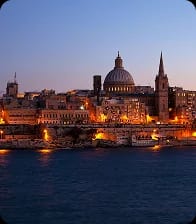 A harbour city skyline lit at dusk, seen across the water from the seafront.