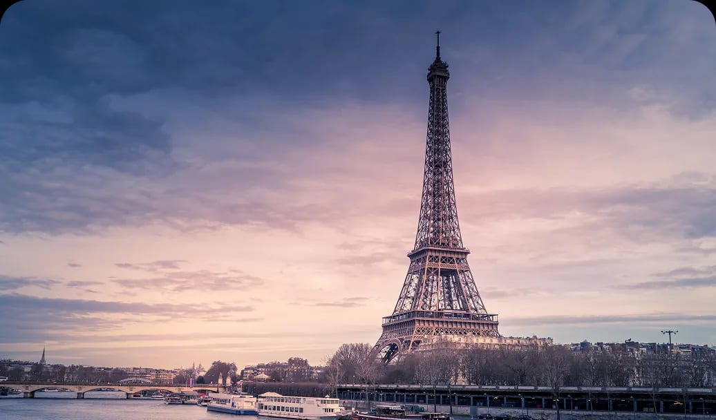 The Eiffel Tower above the Seine at dusk, with river boats moored along the bank.